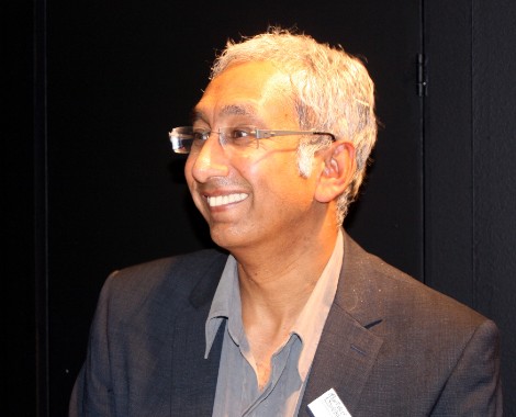 An Asian man with grey hair, wearing glasses and smiling.